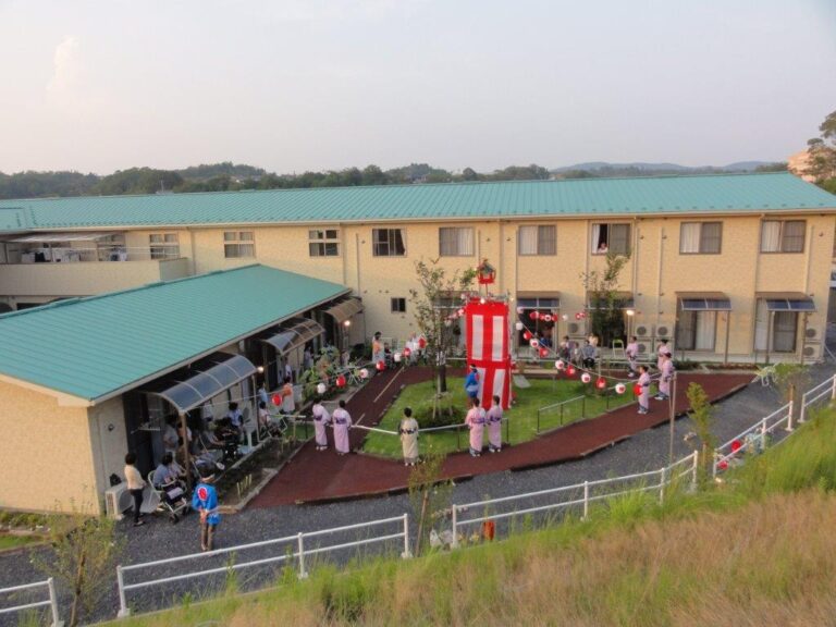 施設の庭園でイベント開催中。入居者と職員が集まり、赤い装飾と共に交流する風景
